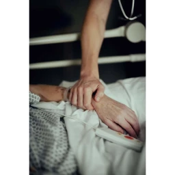 Close-up of a person holding the hand of an elderly patient in a hospital bed, captured by Nicolas Lascourrèges.