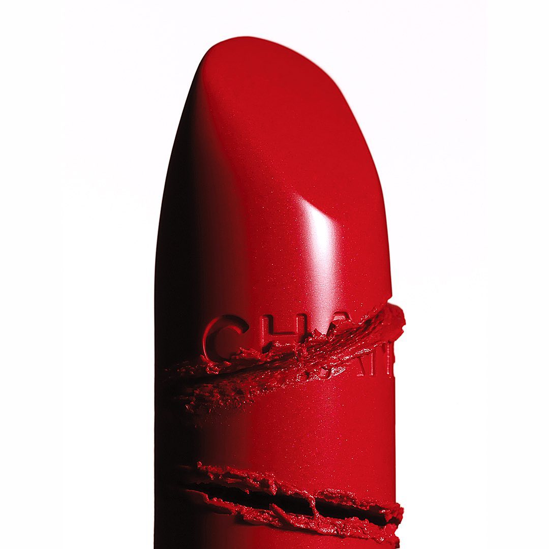 Close-up of a red lipstick tube with the Chanel brand name imprinted on its surface against a white backdrop, beauty product. 