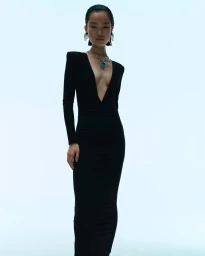 Model in a black V-neck evening gown wearing a statement pendant necklace against a pale seamless background.