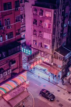 High-angle view of a vibrant city street illuminated by pink and purple neon signs at night with a car and pedestrians below.