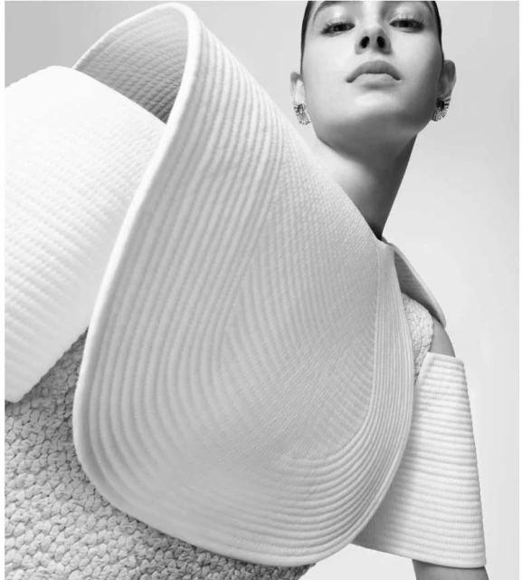 Monochrome portrait of a woman wearing avant-garde textured white dress and jeweled earrings against a bright, neutral backdrop.