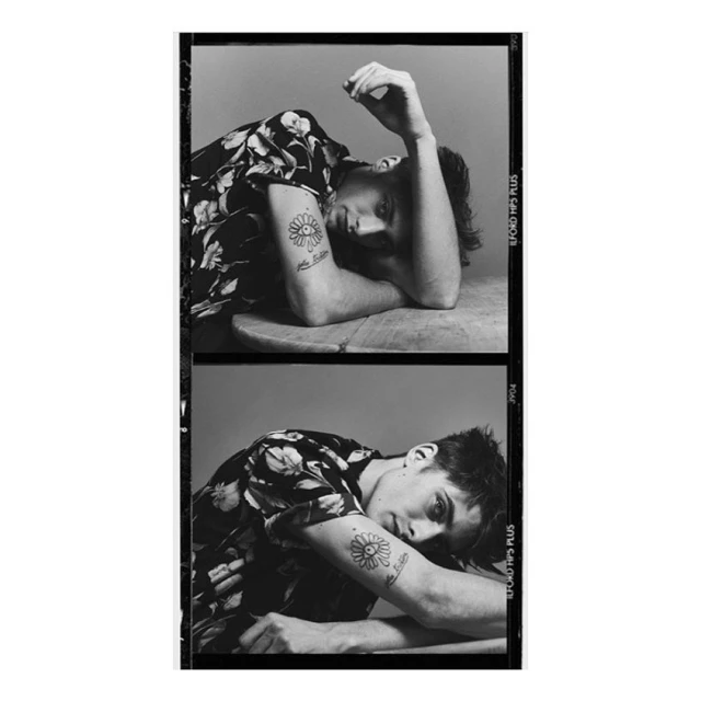 Monochrome portrait of a young adult male with a floral shirt and tattoos, resting his arms on a circular wooden surface in two film frames.
