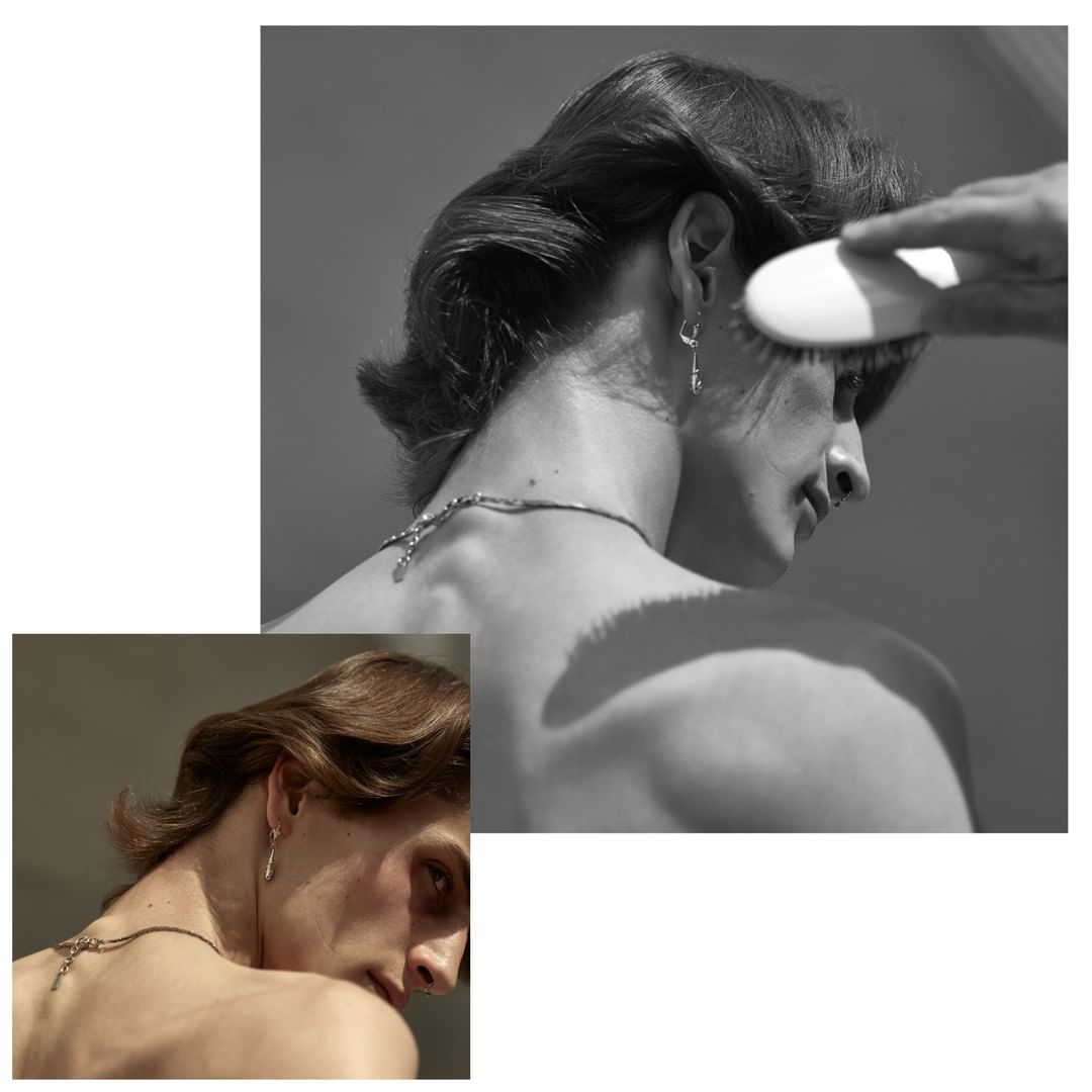 Black and white image of a person with dark hair, jewelry, and a brush near their head, showcasing fashion and beauty elements.