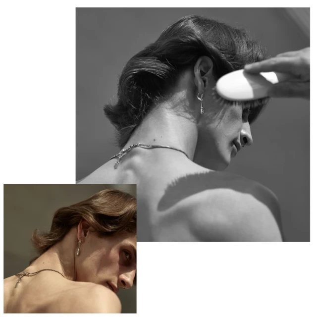 Black and white image of a person with dark hair, jewelry, and a brush near their head, showcasing fashion and beauty elements.