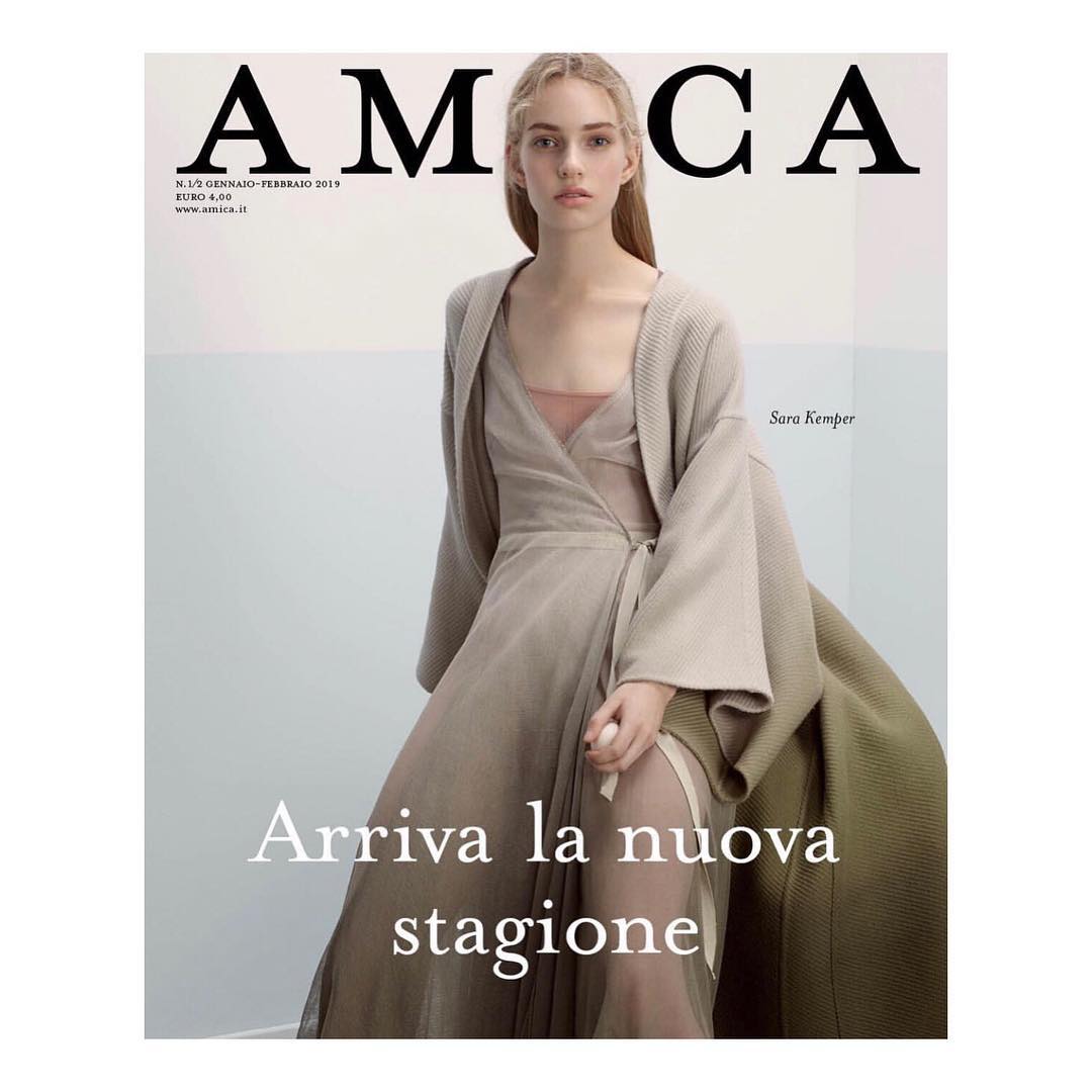 Magazine cover featuring a fair-skinned adult female fashion model wearing a sheer beige dress and a cardigan in a photo studio.