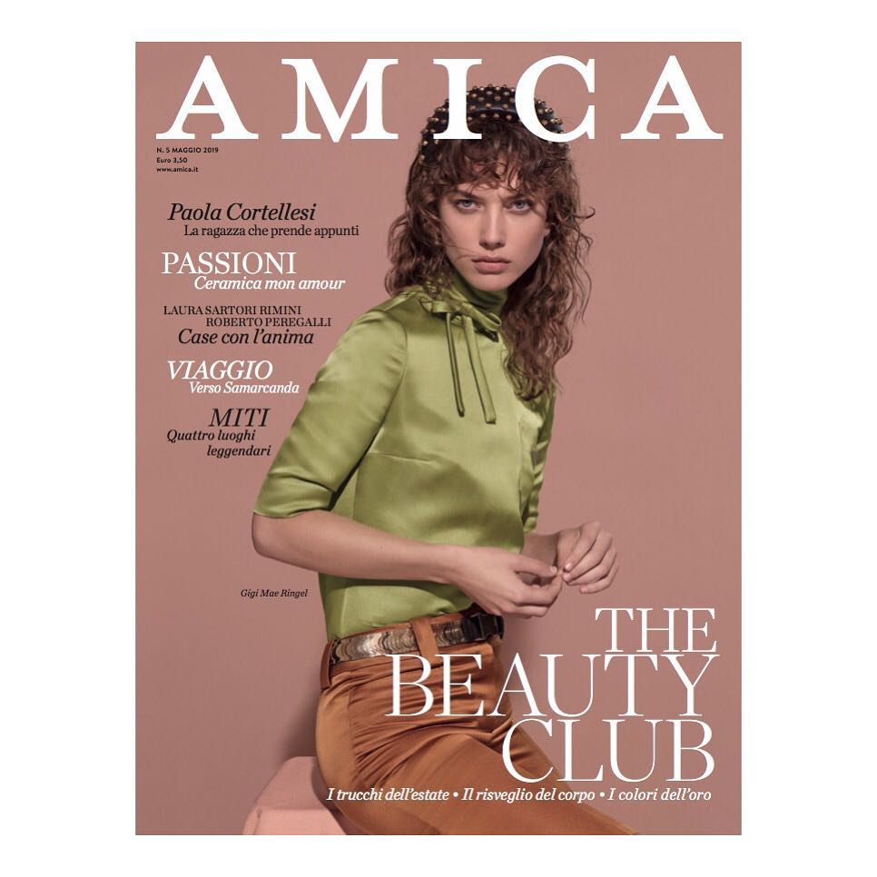 Magazine cover featuring a young female model with curly brown hair, wearing a green satin blouse and brown pants, on a pink background.