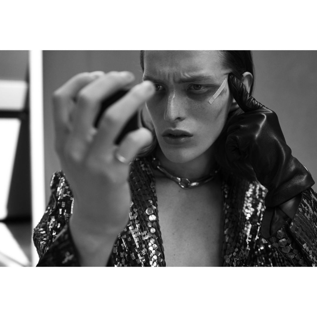 Monochrome fashion portrait of a single model in a sequined jacket and leather gloves, striking a pose in an indoor environment.