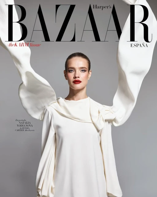 Fashion magazine cover featuring a fair-skinned woman in a white dress with voluminous sleeves and bold red lipstick against a gray background.