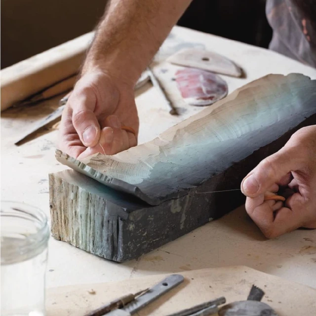 Artisan cutting clay block with wire in studio. Hands working with ceramic, pottery tools, workspace. Handmade craft production concept.