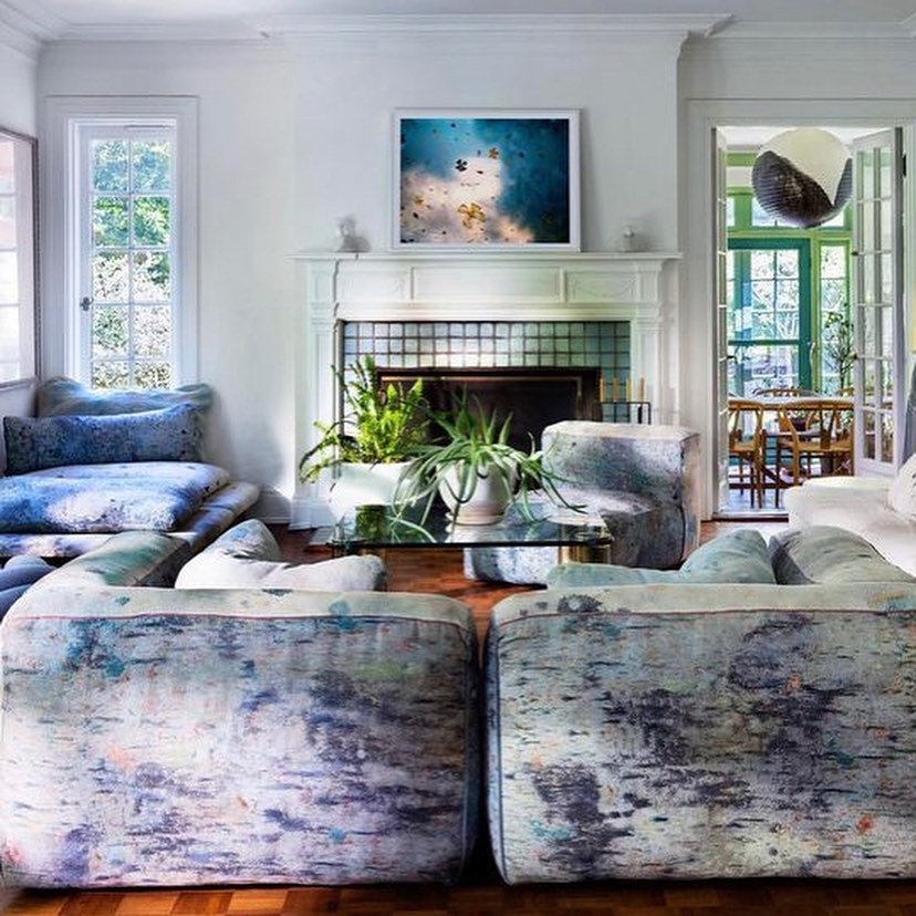 Living room interior with modern, patterned sofas, glass coffee table, fireplace, framed wall art, and view to dining area.