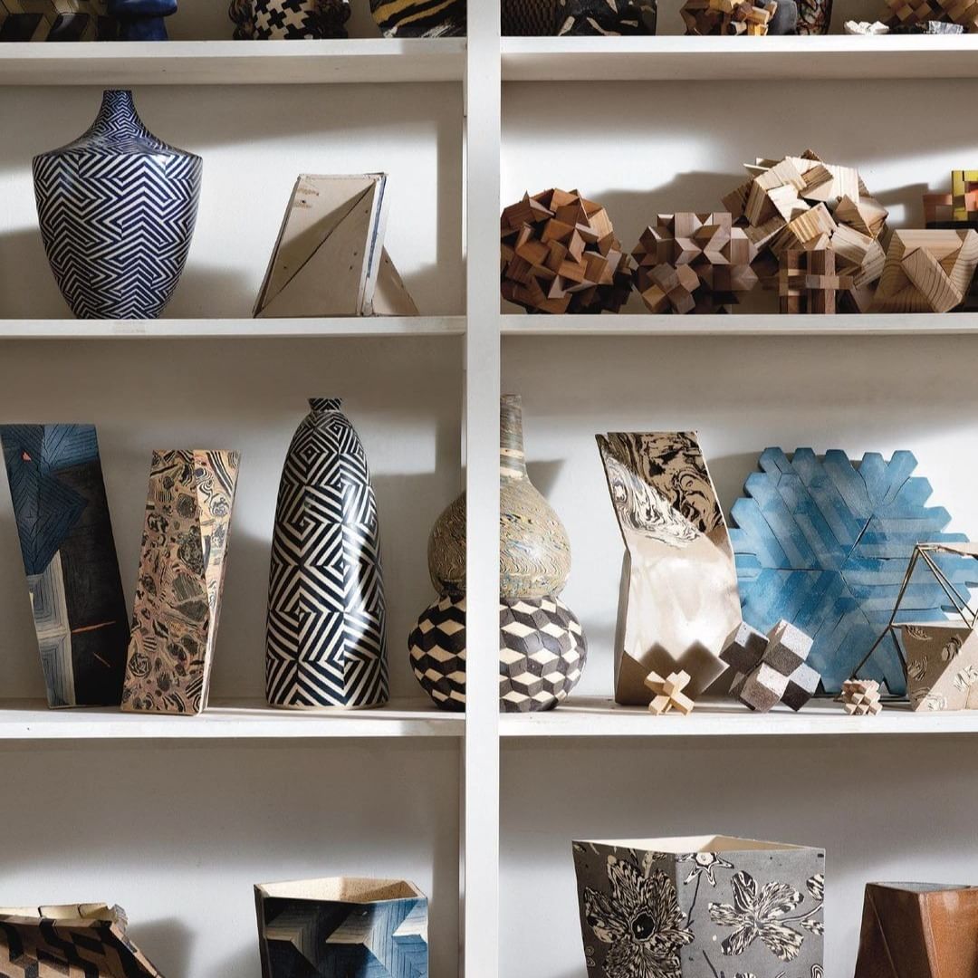 Shelves filled with geometric-patterned pottery and wooden objects in shades of blue, gray, beige, brown, and black and white.