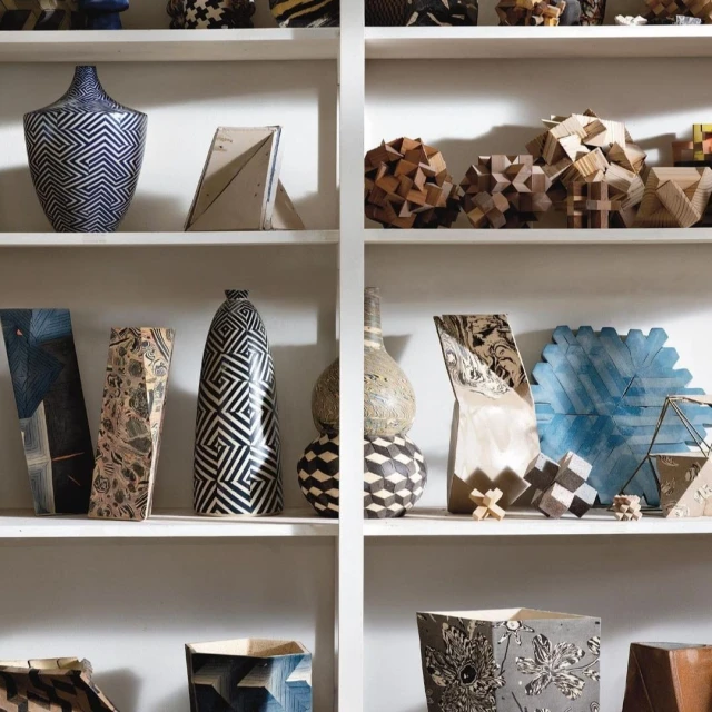 Shelves filled with geometric-patterned pottery and wooden objects in shades of blue, gray, beige, brown, and black and white.