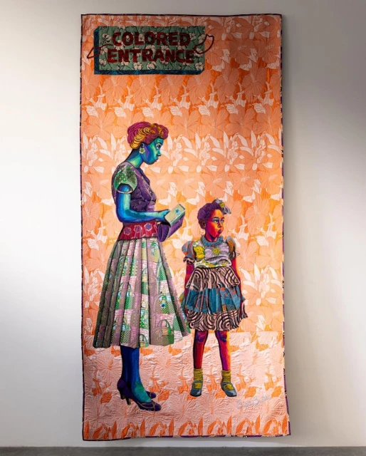 A mixed-media artwork on fabric features an African-American woman and child in a vintage style standing under a "Colored Entrance" sign.