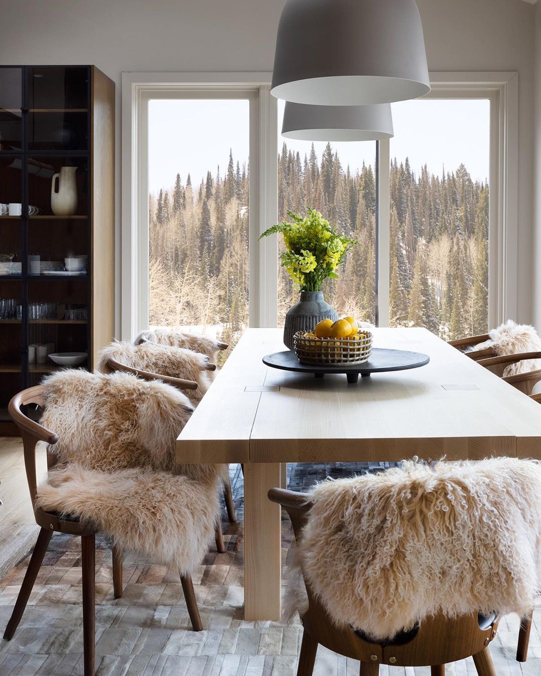 Bright dining room featuring a wooden table set with a floral arrangement and citrus fruit, surrounded by chairs with furry seat covers.