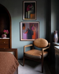 Interior shot featuring a brown leather armchair, two framed abstract paintings on a dark green wall, and wooden furniture.