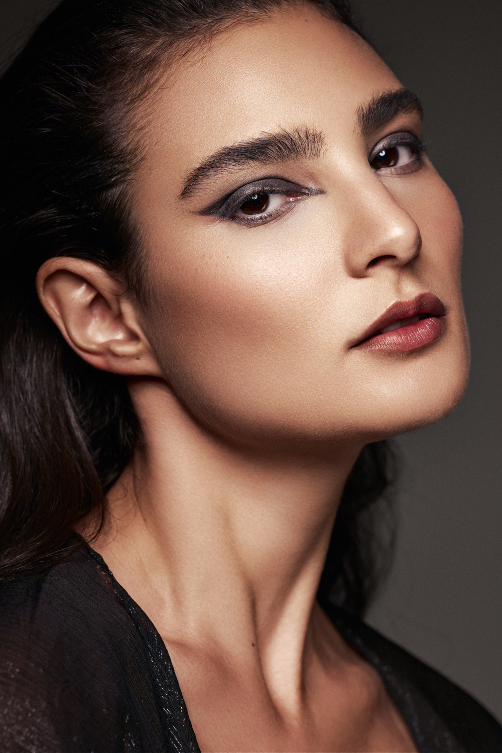 Close-up portrait of a woman with bold graphic eyeliner, arched eyebrows, and dark lips, looking directly at the camera.