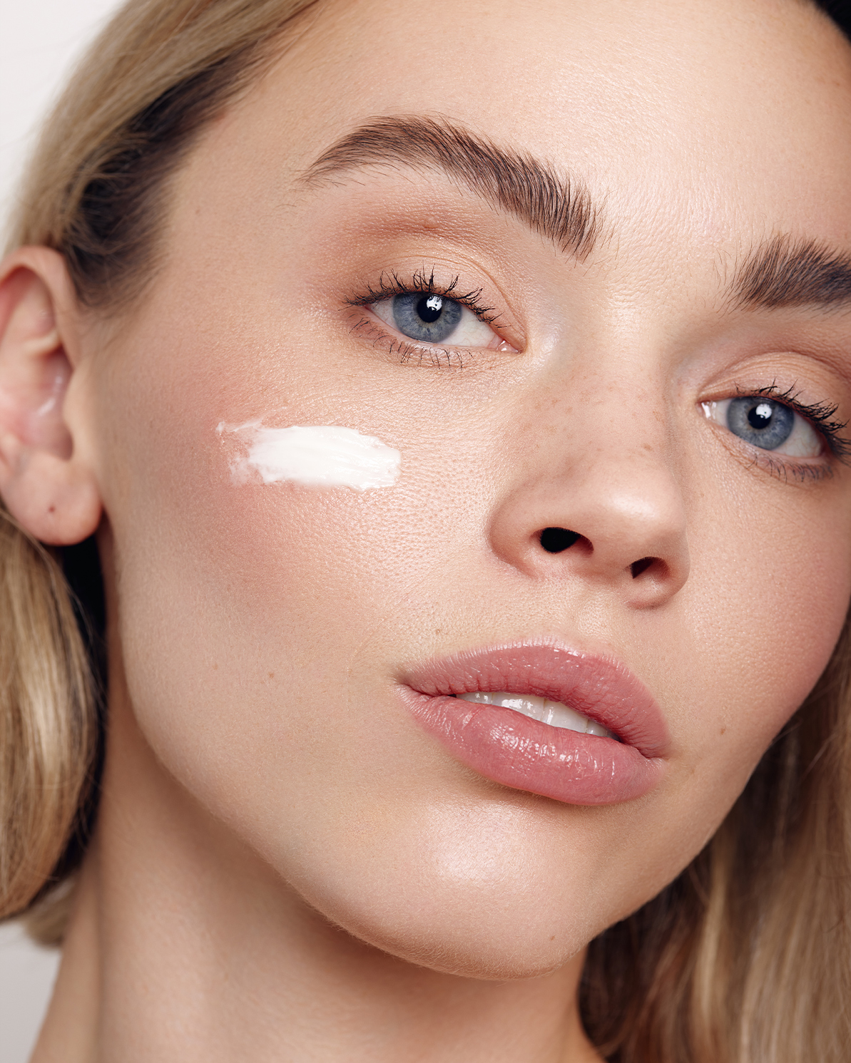 Close-up beauty portrait of a woman with blue eyes and a white cream dabbed on her cheek by retoucher Mariya Dimitrova.