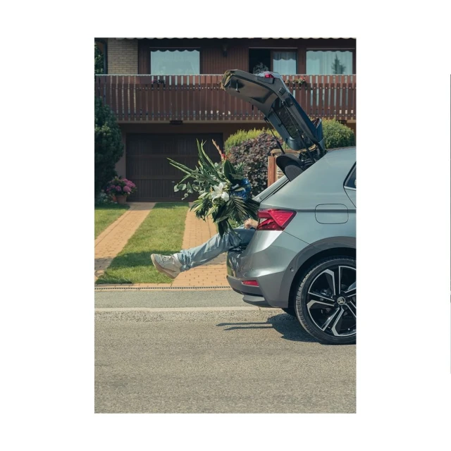 Silver SUV parked outdoors with open hatchback, revealing a person's legs and feet amidst a bouquet of large white flowers.