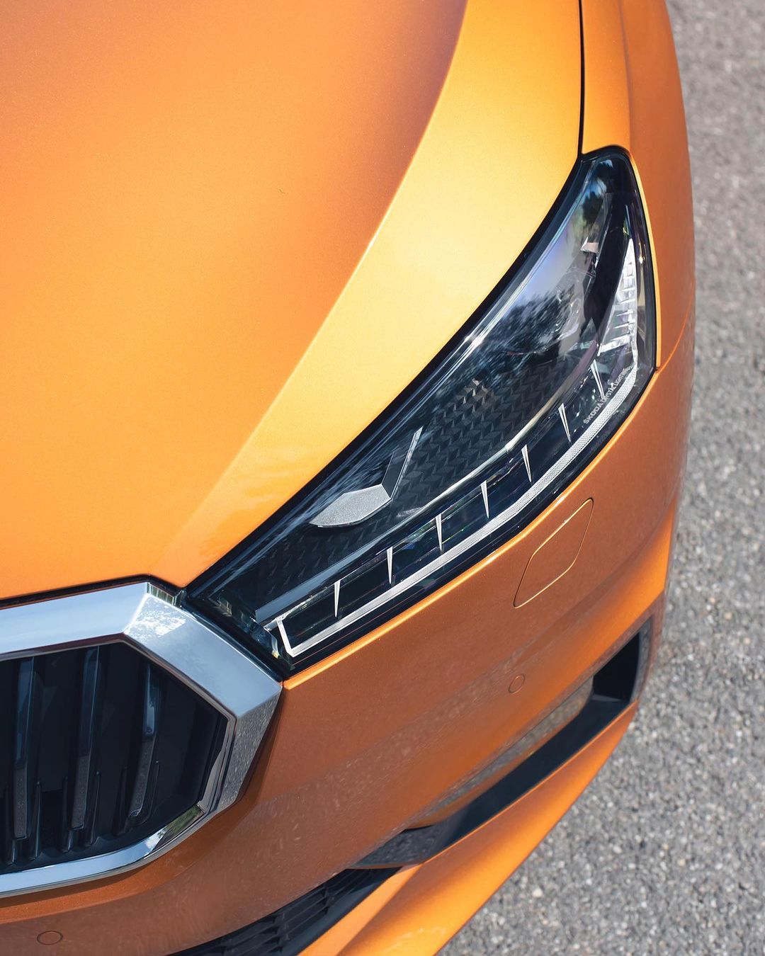 Close-up of the front headlight and grill of an orange Skoda vehicle, showcasing modern automotive design and details.