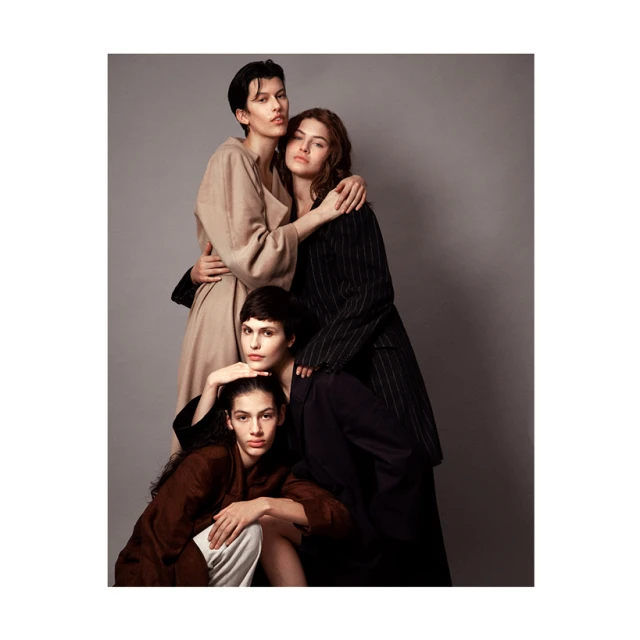 Four women pose in fashionable clothing against a gray background. Models are shown in neutral and brown tones in a studio setting.