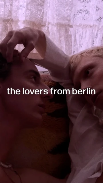 Two adults in close proximity indoors, one hand on the other's face. The scene has a soft, intimate feel with blurred background details.
