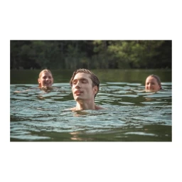 Three young people swimming in a lake, with a man in the foreground and two smiling people in the background water.