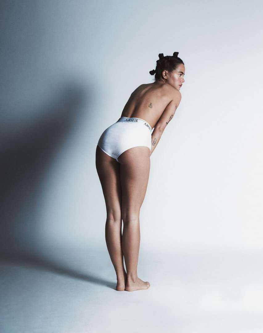 Full shot of a woman with short hair wearing white underwear in a photo studio with bright lighting and shadows.