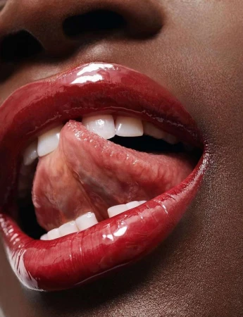 Close-up portrait of an African American adult female, showing lips covered in glossy red lipstick and tongue protruding between teeth.