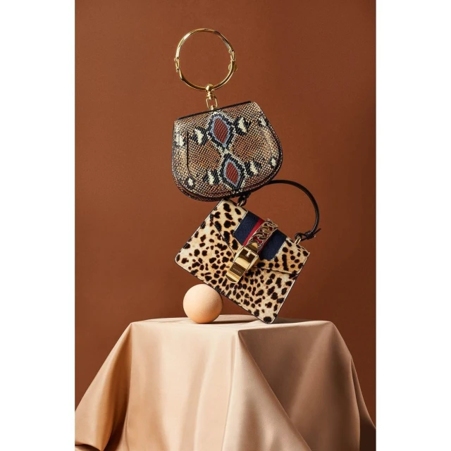 Still life studio shot of two fashion handbags in a stacked arrangement on a draped surface, with a seamless brown backdrop.