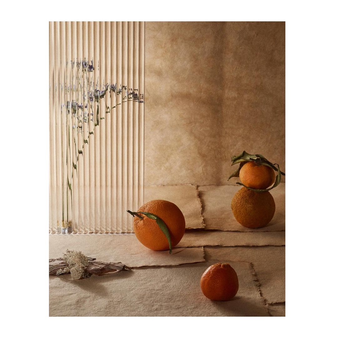 Still life of oranges with leaves on textured paper in studio, creating a natural, rustic food and beverage display with filtered light.