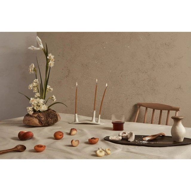Still life of peaches, flowers, and candles arranged on a linen tablecloth in a natural light setting. Neutral color palette and textures.