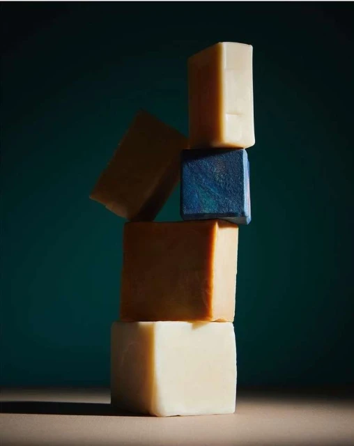 Stack of handcrafted soap bars in various colors and textures against a dark teal background, creating an abstract, organic tower.