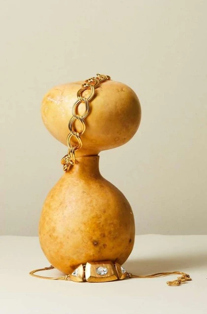 Still life of a gold chain bracelet and necklace draped on a light-colored gourd, shot in a studio with soft lighting and neutral background.
