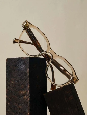 Close-up of stylish eyewear glasses by Raen, featuring clear lenses and a neutral frame, placed on rustic wood blocks.