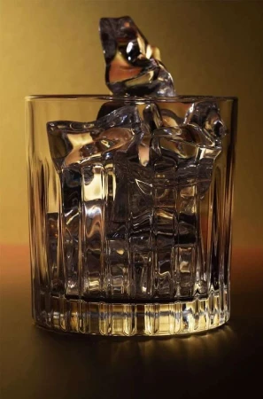 Crystal old fashioned glass filled with clear ice cubes against a warm brown and golden background