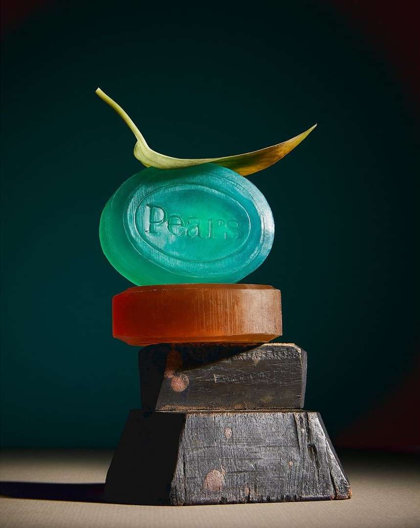 Still life of stacked soap bars from the brand Pears, topped with a leaf. Set against a dark background, the focus is on beauty and cleanliness.