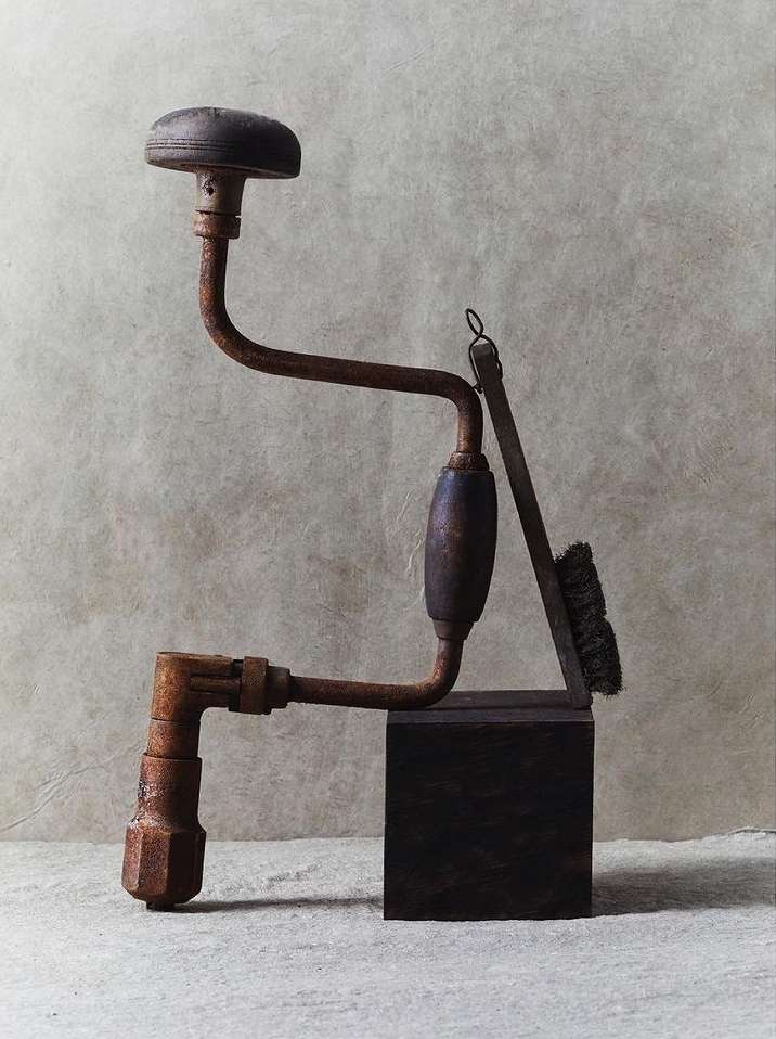 Antique rusty hand drill and brush on wooden block against a neutral backdrop in a studio setting, showcasing aged textures.
