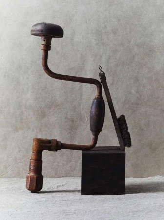 Antique rusty hand drill and brush on wooden block against a neutral backdrop in a studio setting, showcasing aged textures.