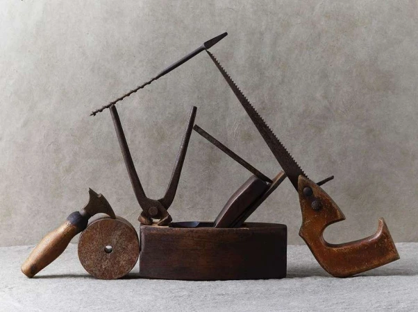 Still life shot of vintage hand tools including saws, metal cutters, and a wooden block plane on a neutral surface.
