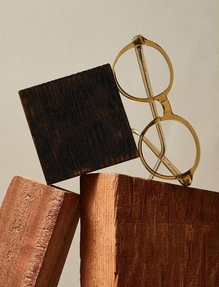 Eyeglasses with gold frames resting on wooden blocks against a neutral background in a still life studio arrangement.