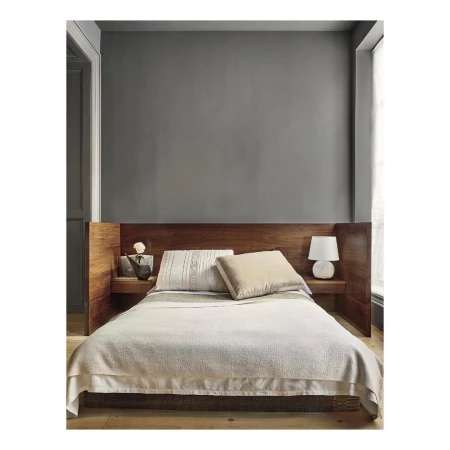 Bedroom interior featuring a queen-size bed with a wooden headboard, white bedding, side table with lamp and decorative items, neutral color palette.