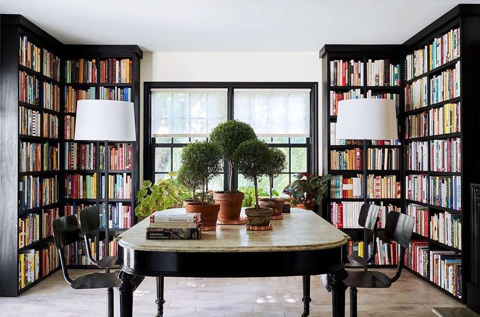 Interior view of a room with black bookshelves filled with colorful books, a marble table with potted plants, and black chairs.
