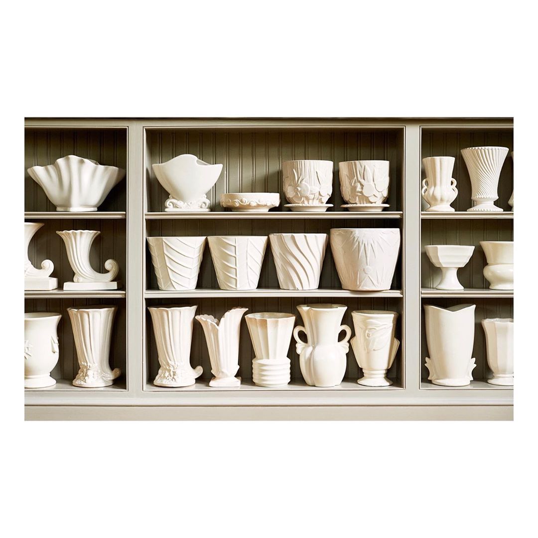 Collection of white ceramic vases and pots arranged on shelves in a display case, showcasing a variety of shapes and textures.