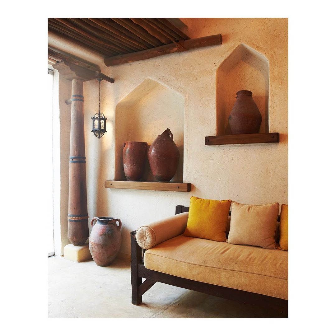 Indoor scene of rustic decor featuring a neutral-toned sofa, vases in wall niches, and a wooden column with decorative bands.