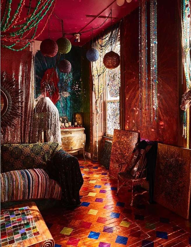 Bohemian style interior with patterned couch, colorful beads hanging from ceiling, mosaic floor, and artistic wall decor.