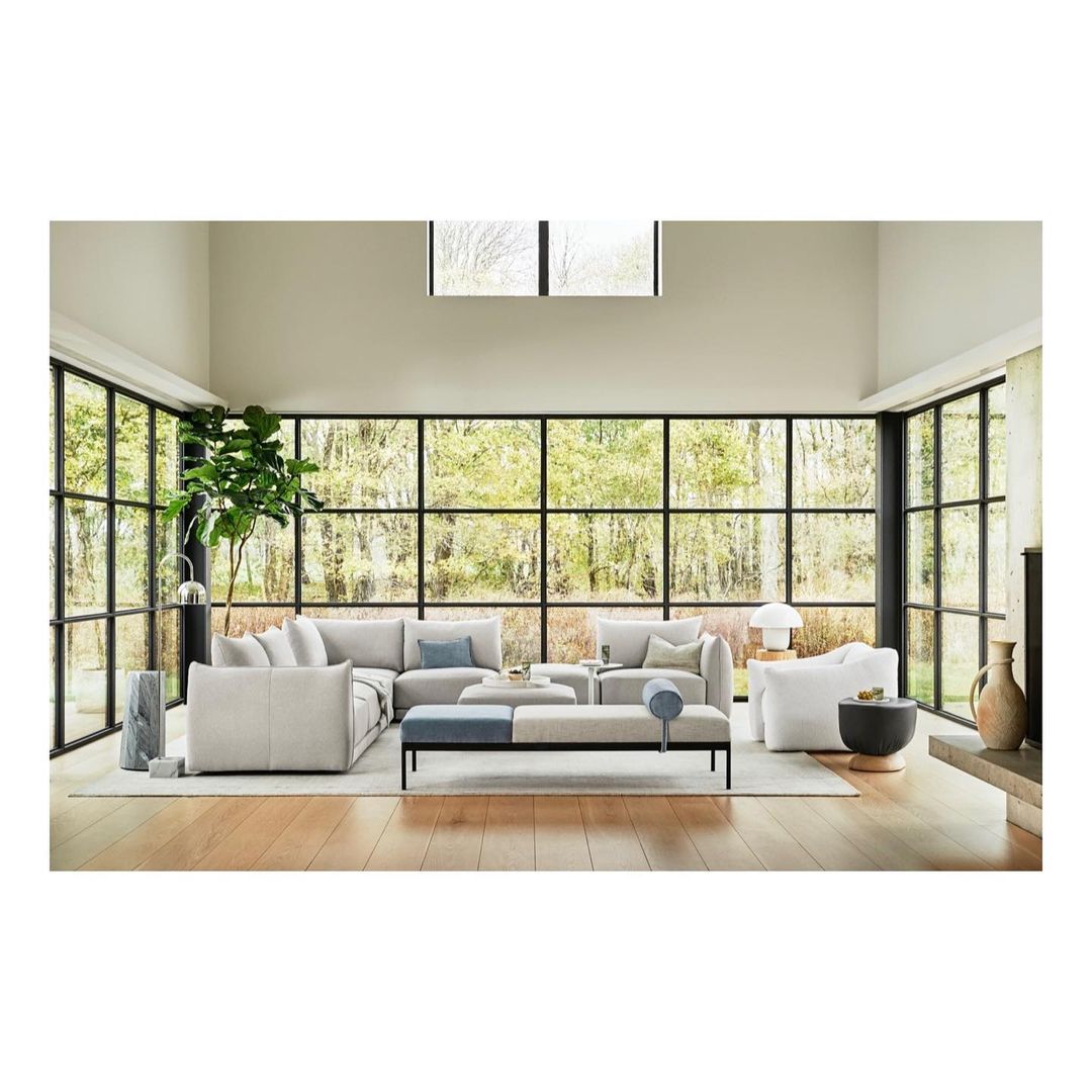 Contemporary living room interior with a large sectional sofa, bench seating, floor-to-ceiling windows, and natural light.
