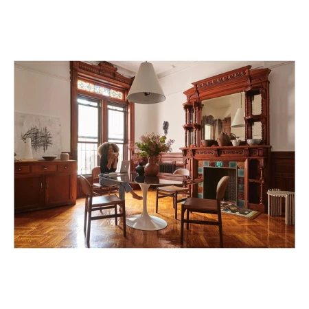 Woman seated at a dining table in a traditional living room with dark wood trim and a large wooden mantelpiece