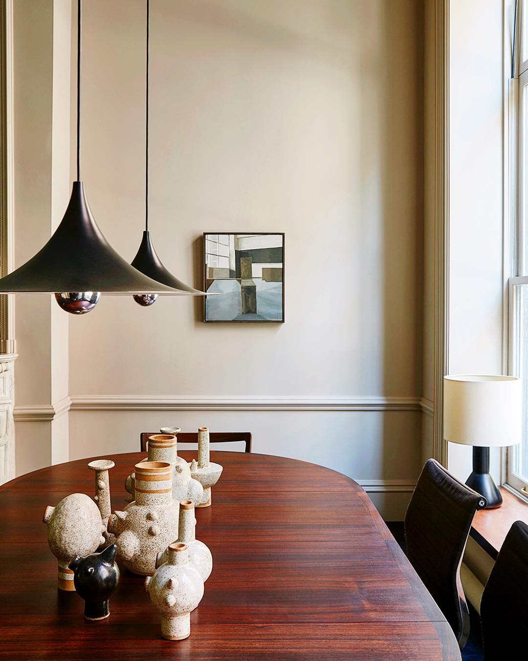 Interior view of dining room featuring a wooden table with ceramic vases, overhead lighting, and a neutral color palette.