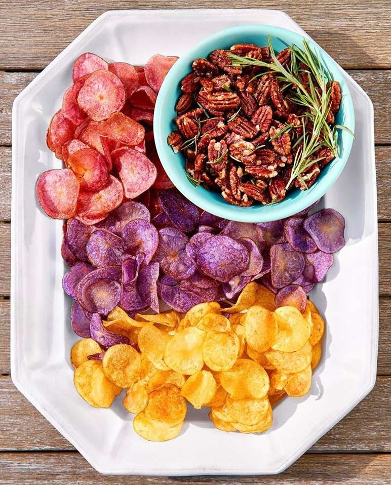Overhead shot of a white tray with potato chips in different colors and a turquoise bowl of pecans, sitting on a wood surface.