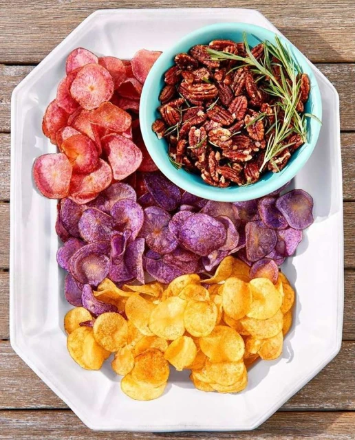 Overhead shot of a white tray with potato chips in different colors and a turquoise bowl of pecans, sitting on a wood surface.